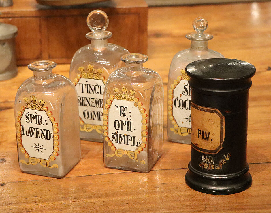 Gläser und Holzdosen, Apotheke Wuppertal-Cronenberg, spätes 18. Jh. An der Holzdose unten ein freigelegter Teil der untersten Farbschicht (Inv.-Nr. II A 84, 85, 87, 88; II G 493, © Deutsche Apotheken Museum-Stiftung, Heidelberg).